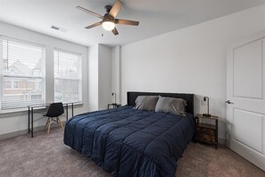 Een slaapkamer met een bed, een bureau, een stoel, een plafondventilator en een raam met jaloezieën.