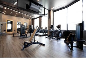 A modern gym with various exercise equipment, large windows, and a brick wall. - Experience Cincinnati! Walkable Modern Condo (Cincinnati)