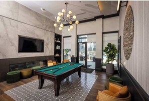 A modern indoor pool area with a pool table, comfortable seating, and a large window offering a view of the outdoors.