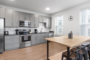 A modern kitchen with grey cabinets, stainless steel appliances, and a wooden dining table with bar stools.
