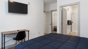 A bedroom with a bed, a desk, a chair, a TV, and a bathroom visible through an open door. - Explore Cincinnati’s Best from a Chic Condo (Cincinnati)