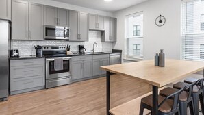 A modern kitchen with grey cabinets, stainless steel appliances, and a wooden dining table with bar stools. - Explore Cincinnati’s Best from a Chic Condo (Cincinnati)
