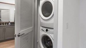 A laundry room with two stacked front-loading washing machines and a closed door. - Explore Cincinnati’s Best from a Chic Condo (Cincinnati)