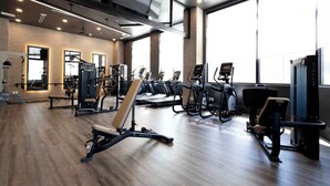 A modern gym with various exercise equipment, large windows, and a brick wall. - Stay Where It’s Happening! Chic Cincy Condo (Cincinnati)