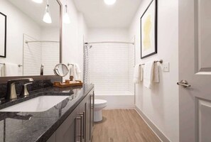 Et moderne badeværelse med en marmorvask, en brusekabine i glas og et toilet.