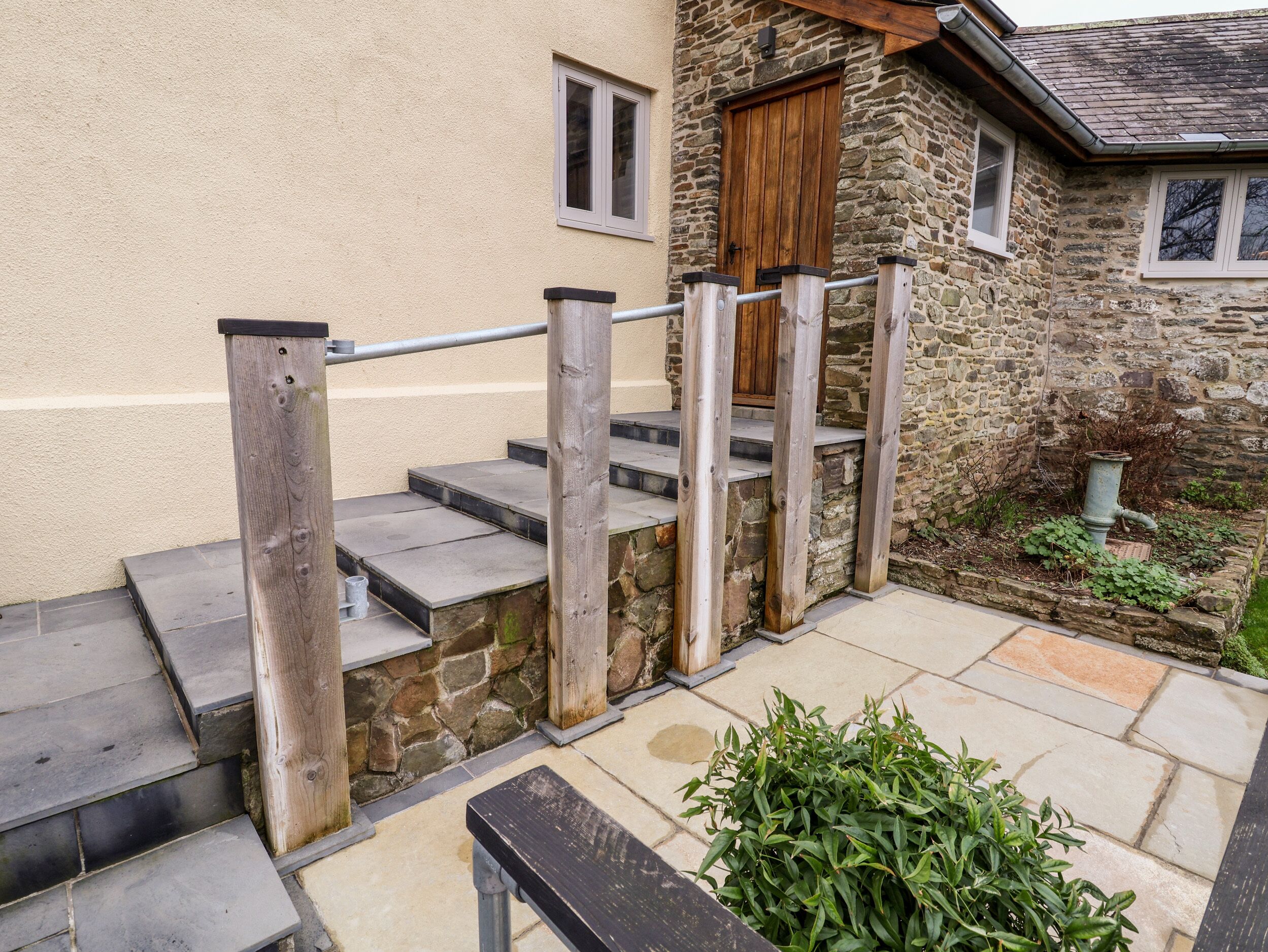 A stone staircase leading to a wooden door, with a metal handrail and steps made of stone slabs.