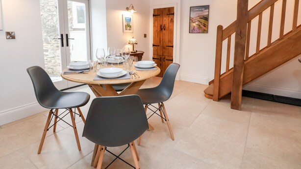 Een eetgedeelte met een houten tafel voor vier personen, omringd door moderne stoelen. Een trap met houten leuningen is rechts zichtbaar.