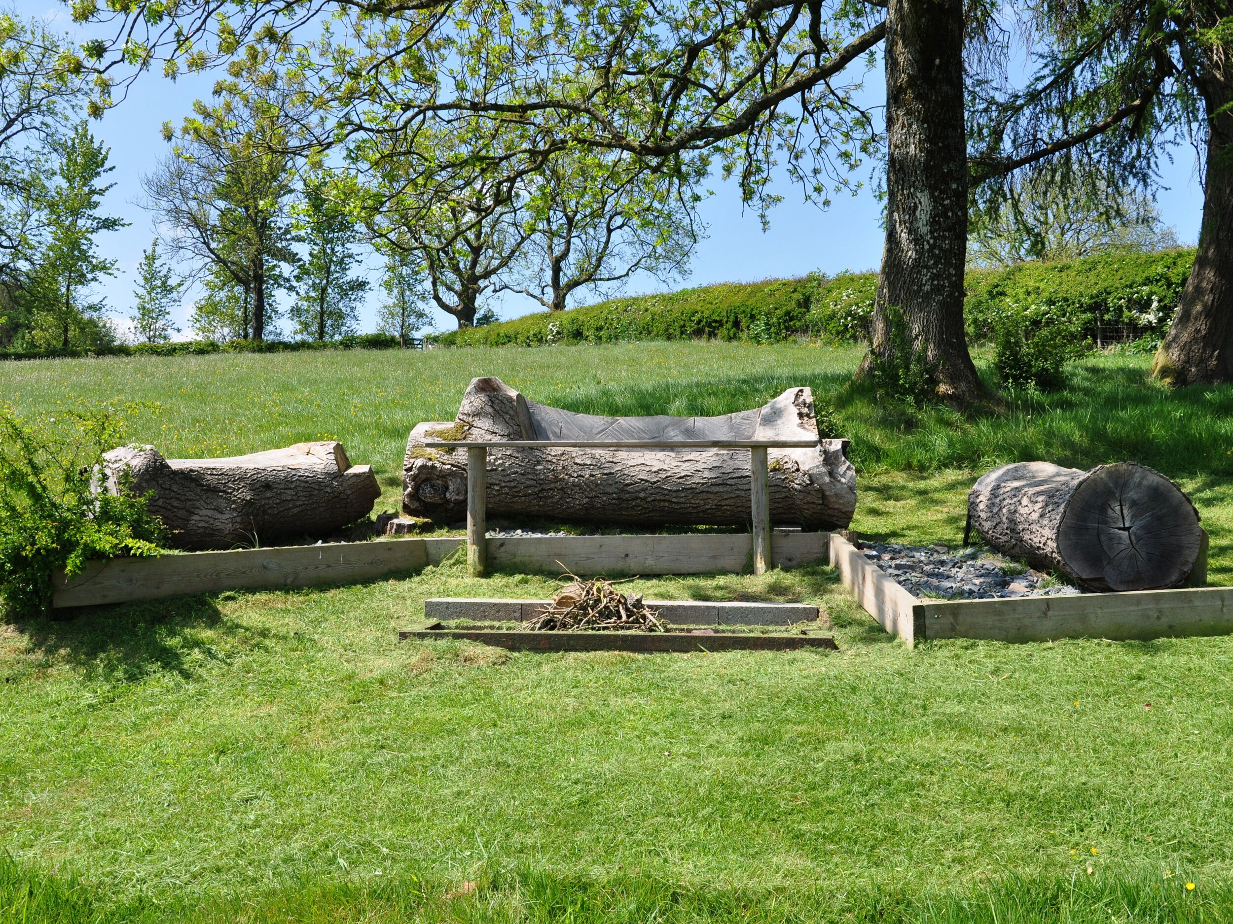Un espace extérieur aménagé de façon naturelle, avec des troncs d’arbres et des structures en bois, qui fait probablement partie d’un parc ou d’un jardin.