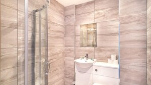Moderni kylpyhuone, jossa on lasinen suihkuseinä, pesuallas, jossa on hygieniatuotteita, ja wc.