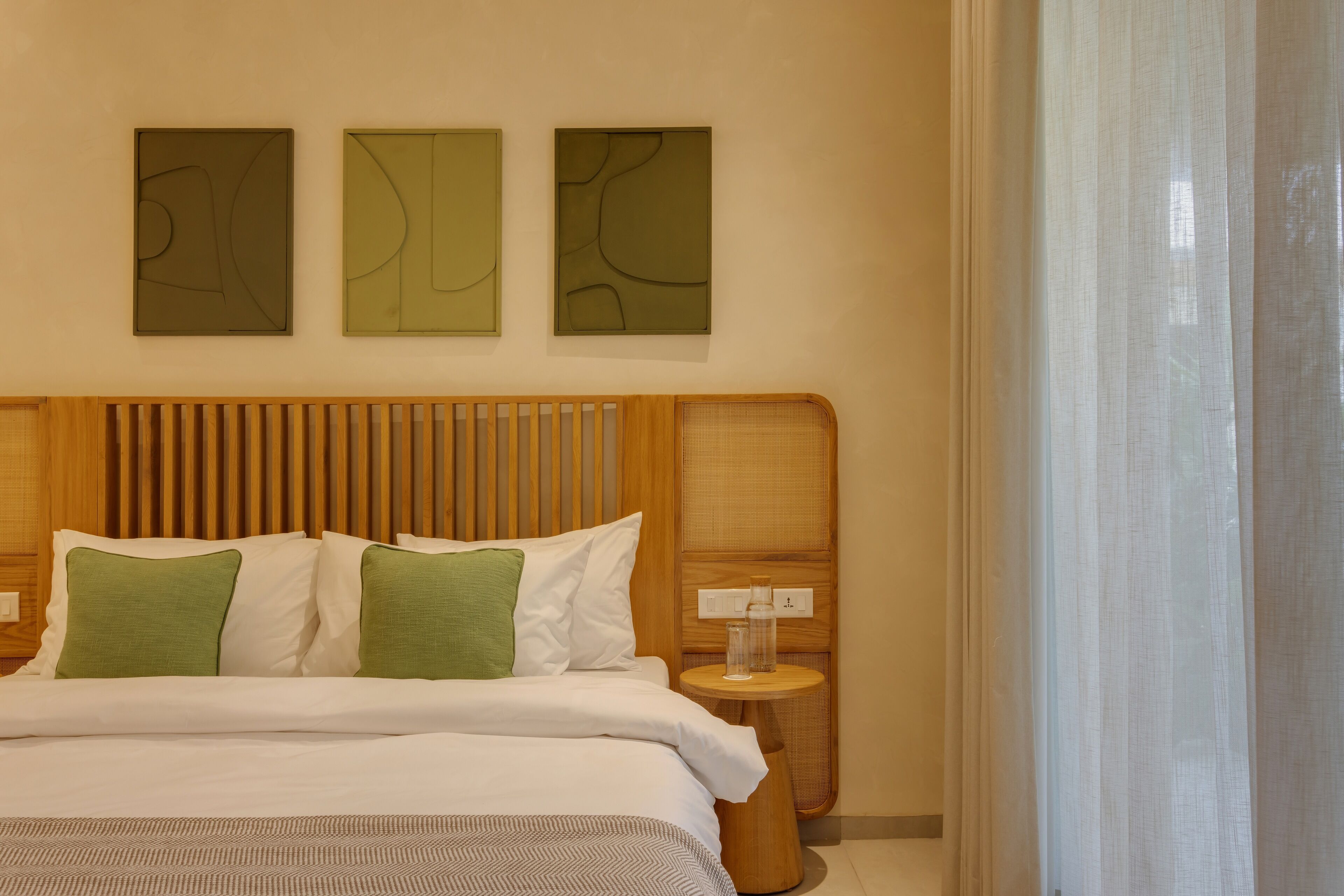 Une chambre d’hôtel avec une tête de lit en bois, un lit avec une literie blanche et verte, et trois œuvres d’art abstraites accrochées au mur.