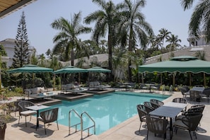 Área de piscina com espreguiçadeiras, guarda-sóis e piscina transparente.
