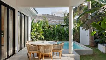 Un patio techado con una mesa y sillas redondas, una piscina y exuberante vegetación tropical.