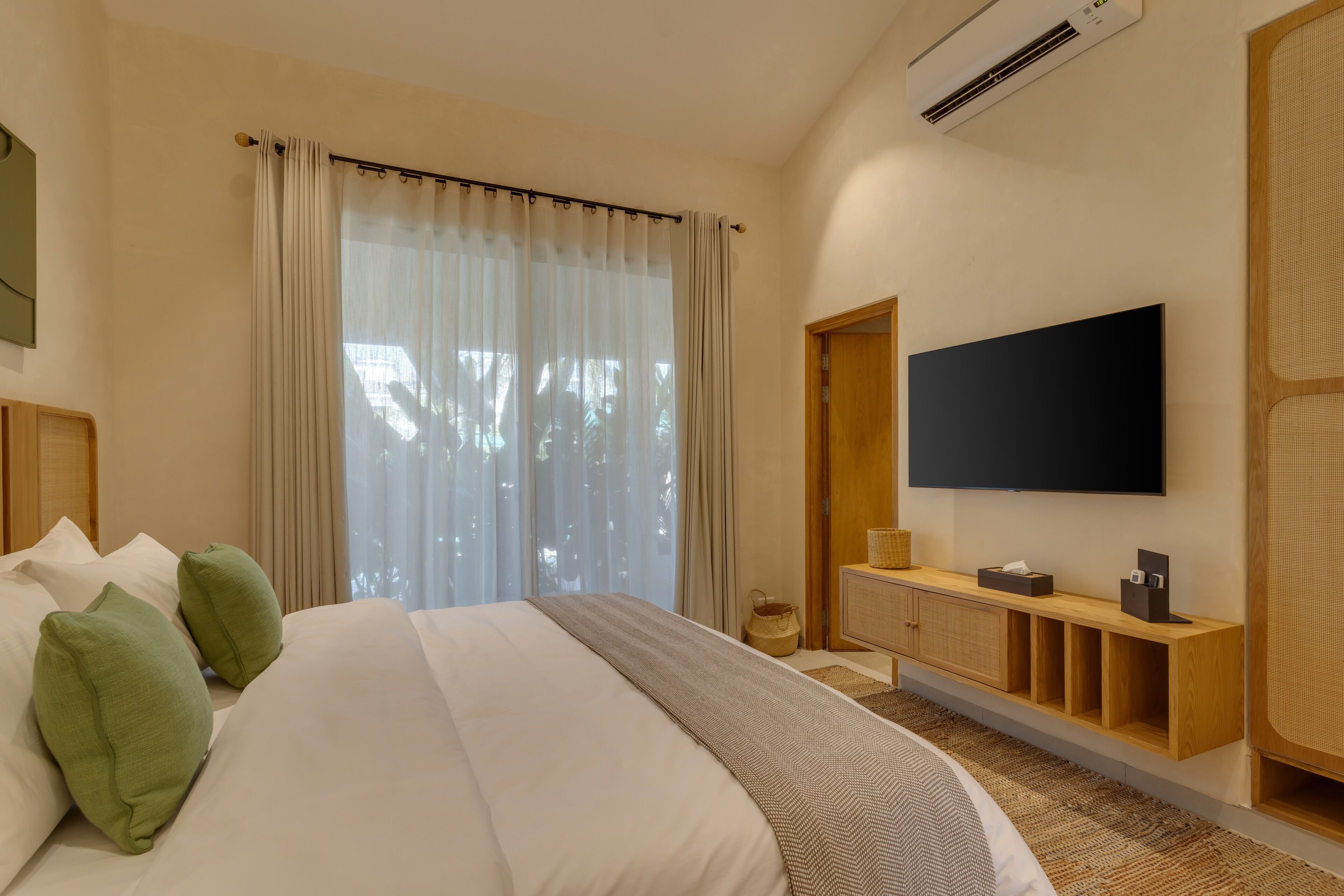 Quarto de hotel moderno com uma cama grande, uma televisão de tela plana na parede, uma mesa de console de madeira e uma janela ampla com cortinas leves.
