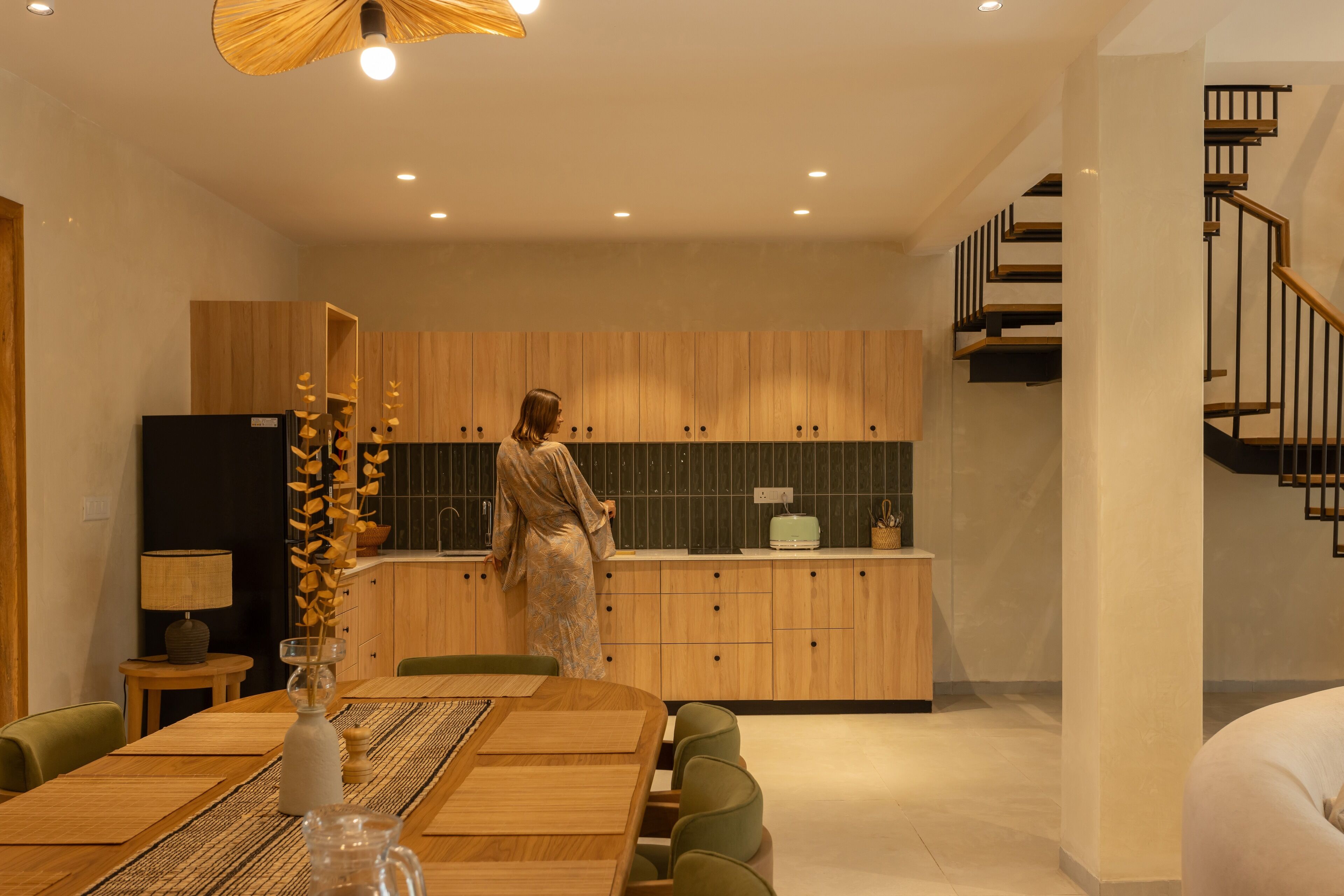Una cocina moderna con armarios de madera, un comedor con mesa y sillas de madera, y una escalera que lleva a un nivel superior.