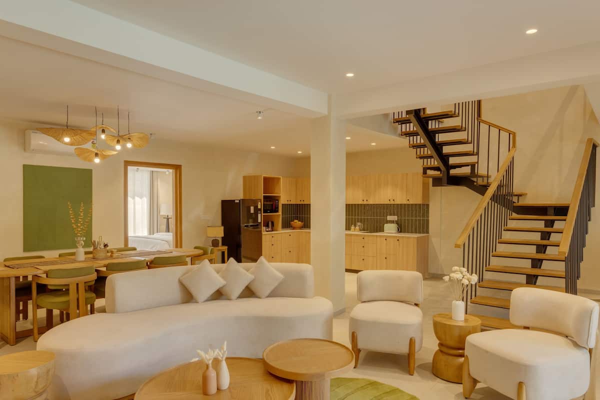 A modern living room with a sofa, chairs, a dining table, and a staircase leading to the upper floor.