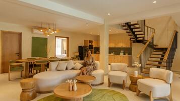 Amplia sala de estar con sofá, mesa de centro y sillas, zona de comedor con mesa y sillas, y cocina con armarios y una escalera.