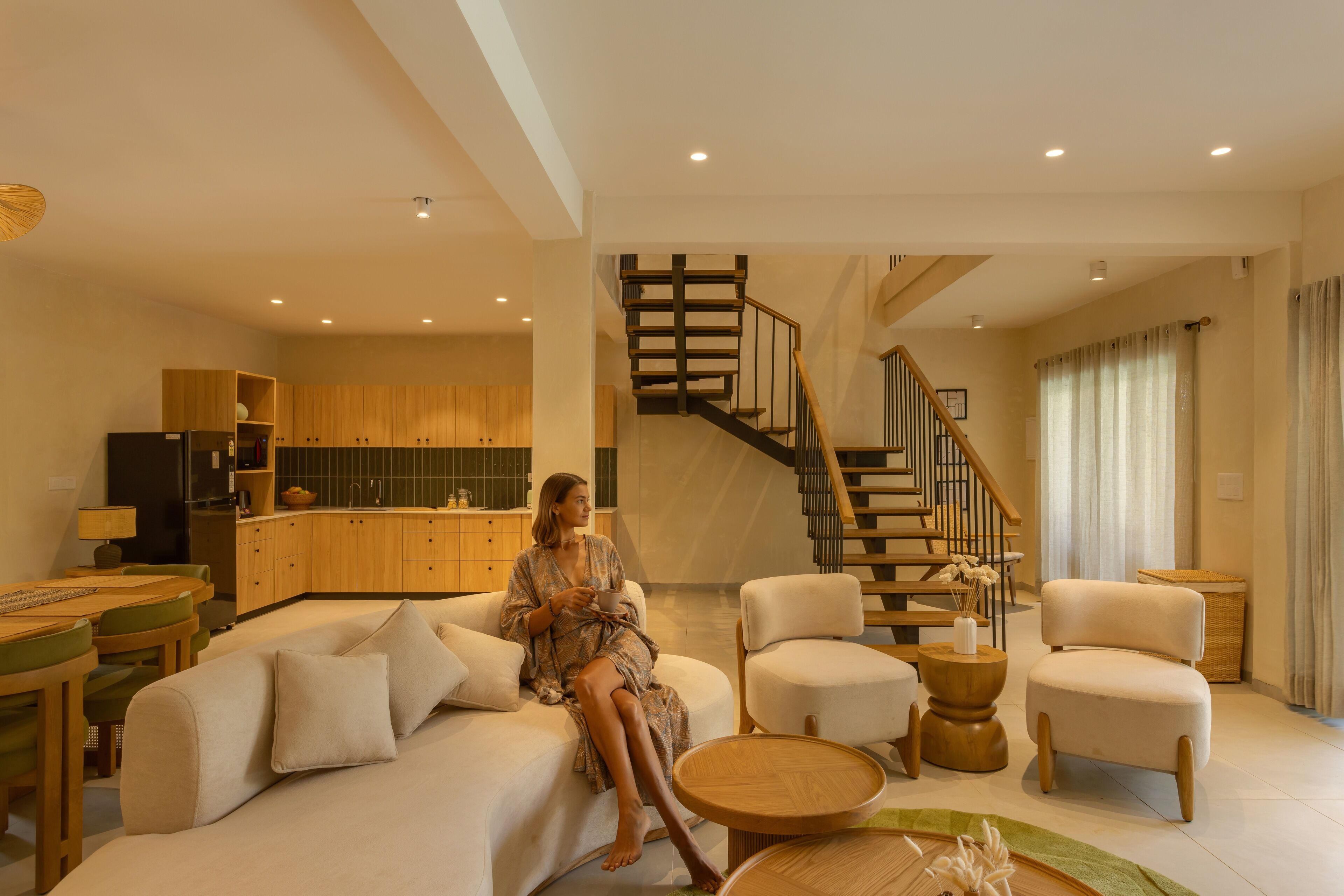 A modern living room with a sofa, chairs, a coffee table, and a staircase.