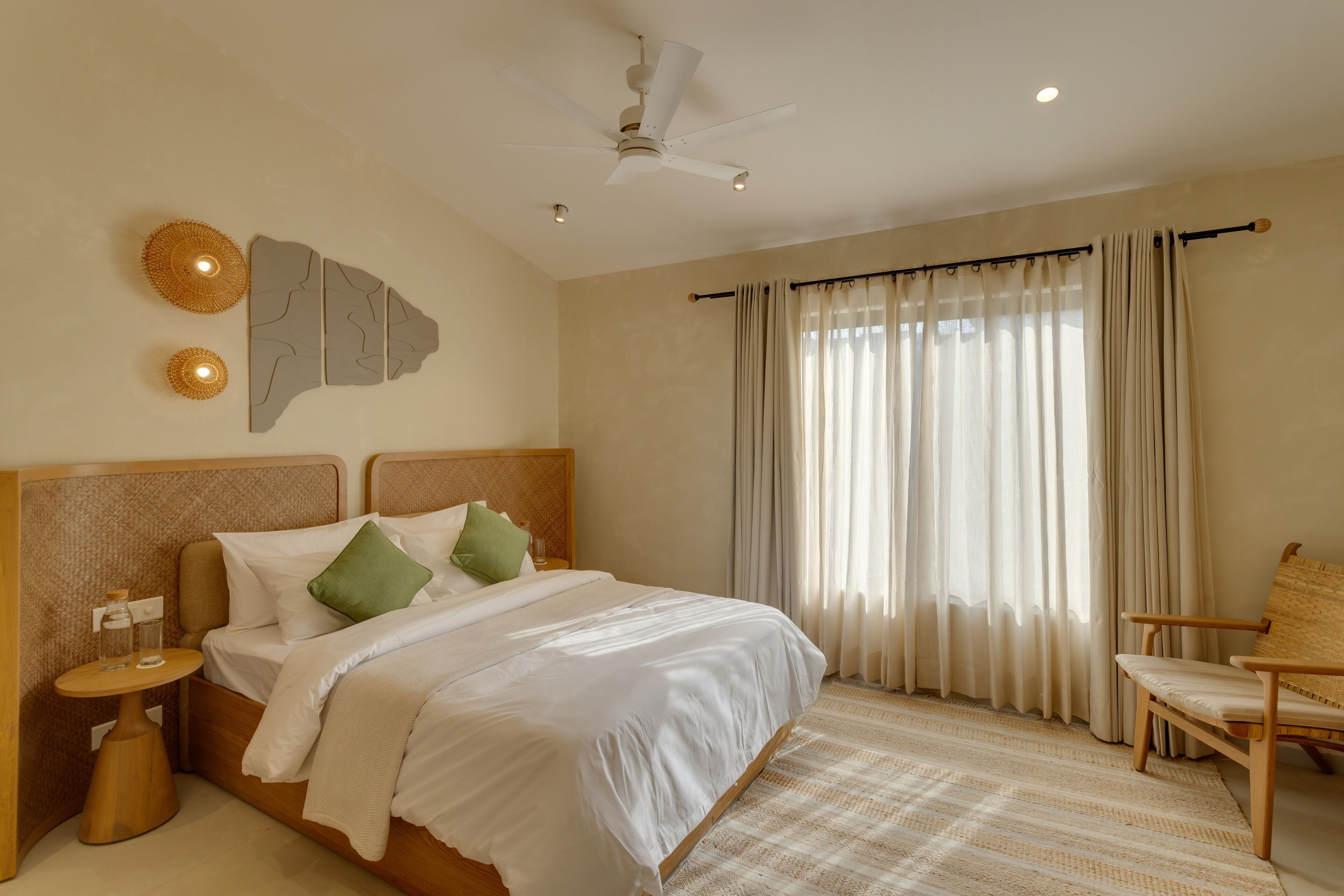 A neatly arranged bedroom with a bed, a chair, a nightstand, a ceiling fan, and a window with curtains.
