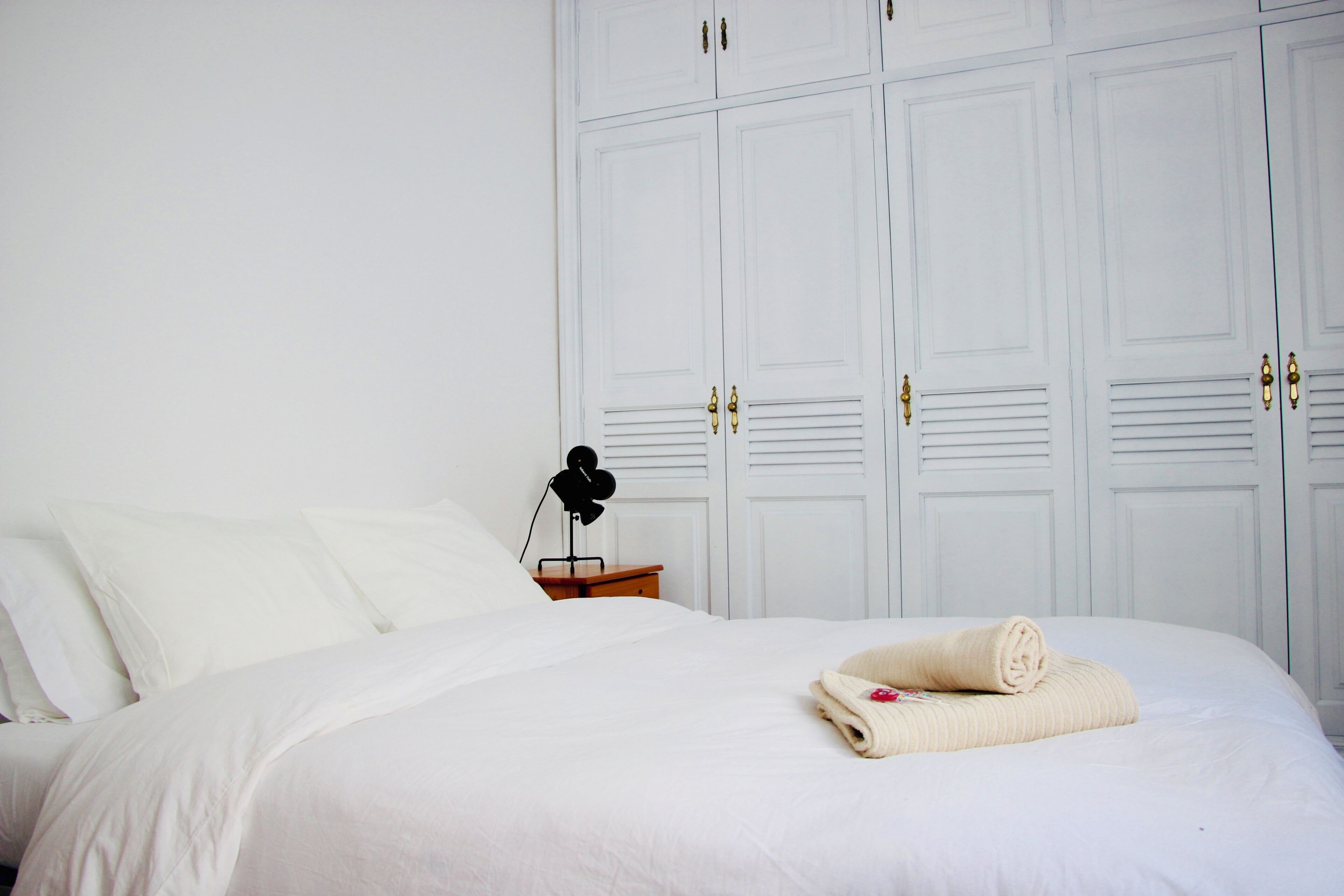 A neatly made bed with white linens, a bedside lamp, and a rolled towel on the bed.