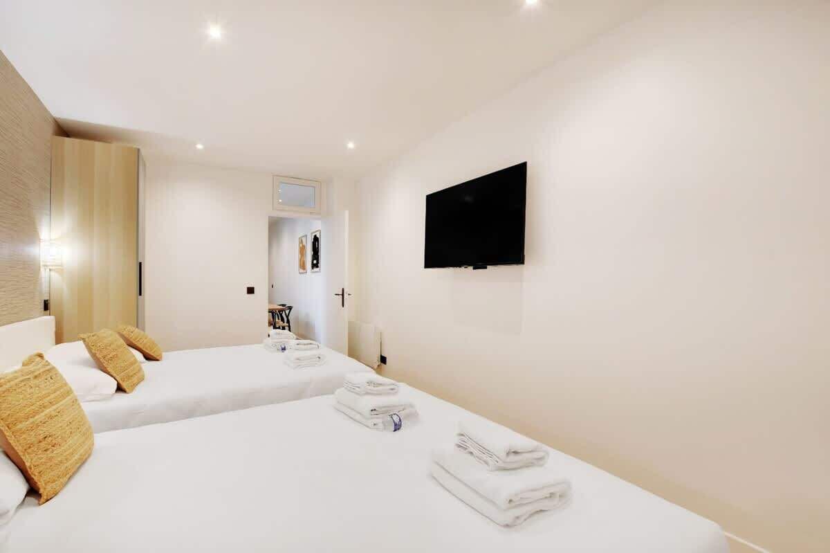 Une chambre d’hôtel avec deux lits, un téléviseur à écran plat et une salle de bain visible par une porte ouverte.