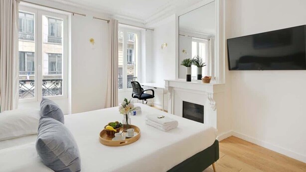 A hotel room with a bed, a TV, a fireplace, and a balcony view. - Renovated and modern 4BD for 12 guests! (Paris)