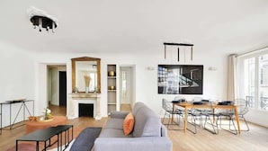 A modern living room with a sofa, dining table, chairs, and a fireplace. - Renovated and modern 4BD for 12 guests! (Paris)