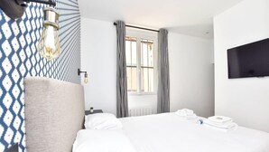 A modern hotel room with a large bed, a flat-screen TV mounted on the wall, and a window with striped curtains. - Modern 2BD apartment in Parc Belleville (Paris)