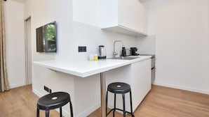 A modern kitchen with white cabinetry, a built-in stove, and a large island with stools. - Modern 2BD apartment in Parc Belleville (Paris)
