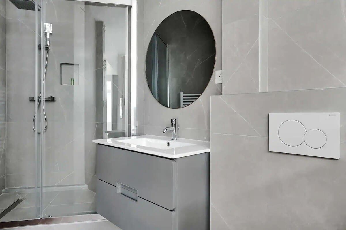 A modern bathroom with a glass shower enclosure, a white sink, and a large mirror.