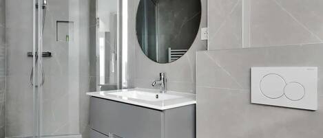 A modern bathroom with a glass shower enclosure, a white sink, and a large mirror.