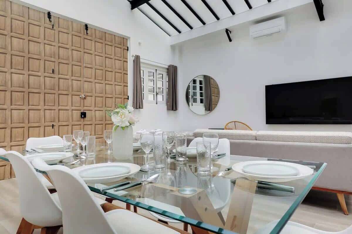 A dining area with a glass table, white chairs, and a sofa.