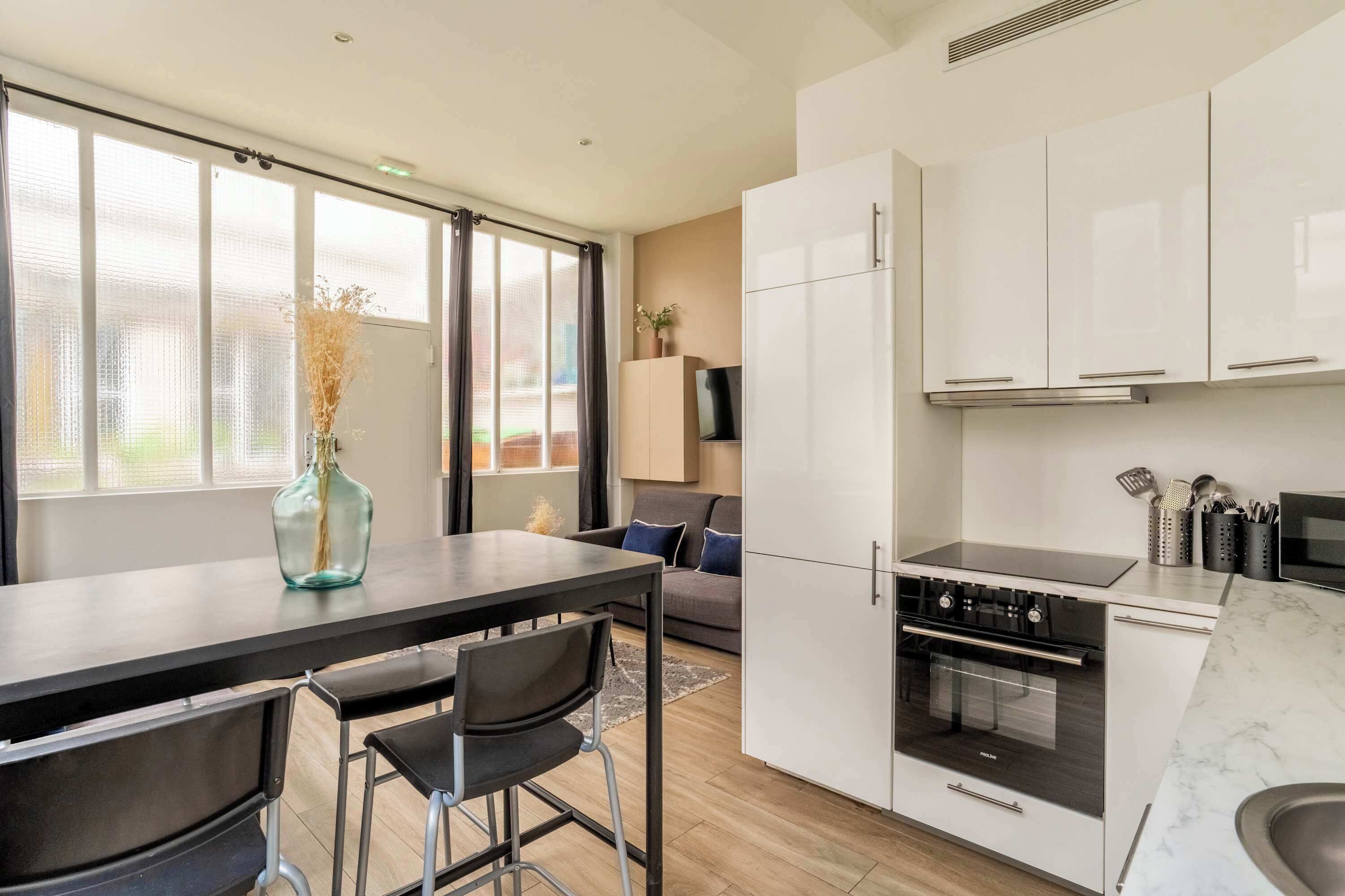 A modern kitchen with a dining area, large windows, and a built-in oven.