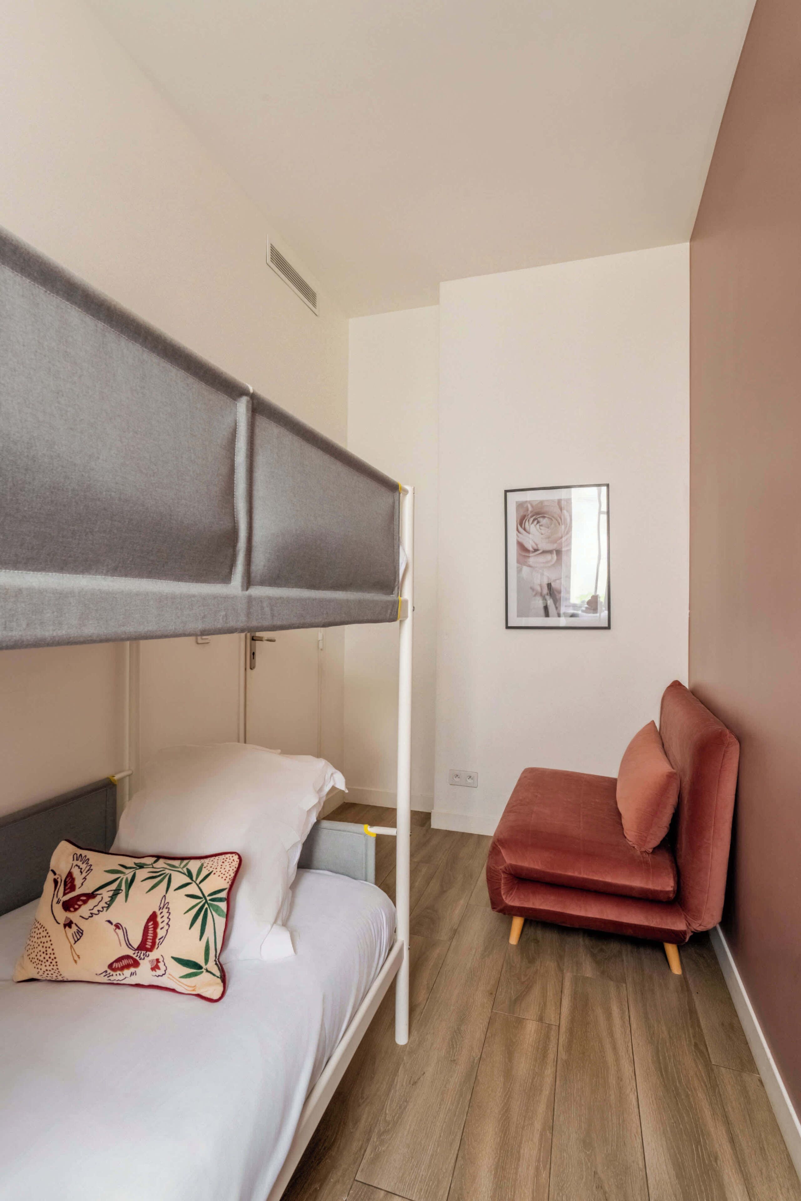 A bunk bed with a grey canopy, a red chair, and a framed picture on the wall.