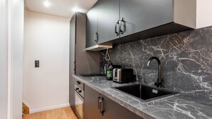 Uma cozinha compacta com armários escuros, bancada de mármore e pia preta.