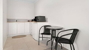 A compact kitchen with white cabinets, a black microwave, and two black chairs around a small round table. - Studio 38 by Tiny Away (Myocum)