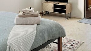 A bedroom with a bed, a TV on a wooden cabinet, a ceiling fan, a window, and a door leading outside. - Studio 38 by Tiny Away (Myocum)