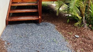 A wooden deck with steps leading to a porch, surrounded by tropical plants and a palm tree. - Studio 38 by Tiny Away (Myocum)