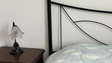 Un lit avec une couette à motifs nuageux, une table de chevet avec une lampe et une tête de lit en métal noir, le tout placé devant un mur uni.