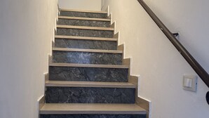 Een trap met marmeren treden en een houten leuning, die uitkomt op een plateau met een lichtschakelaar en een intercom bevestigd aan de muur.