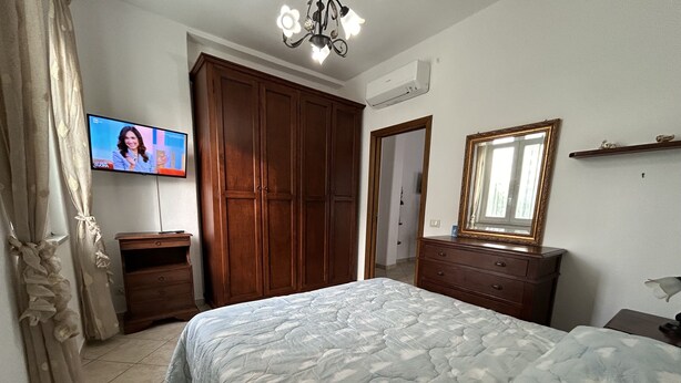 Een slaapkamer met een bed, een houten garderobe, een televisie en een spiegel.