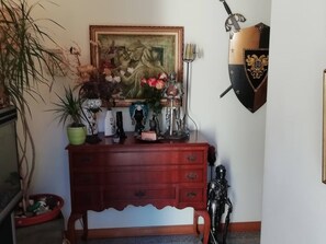 Un aparador de madera con cajones, un cuadro encima y un escudo en la pared.