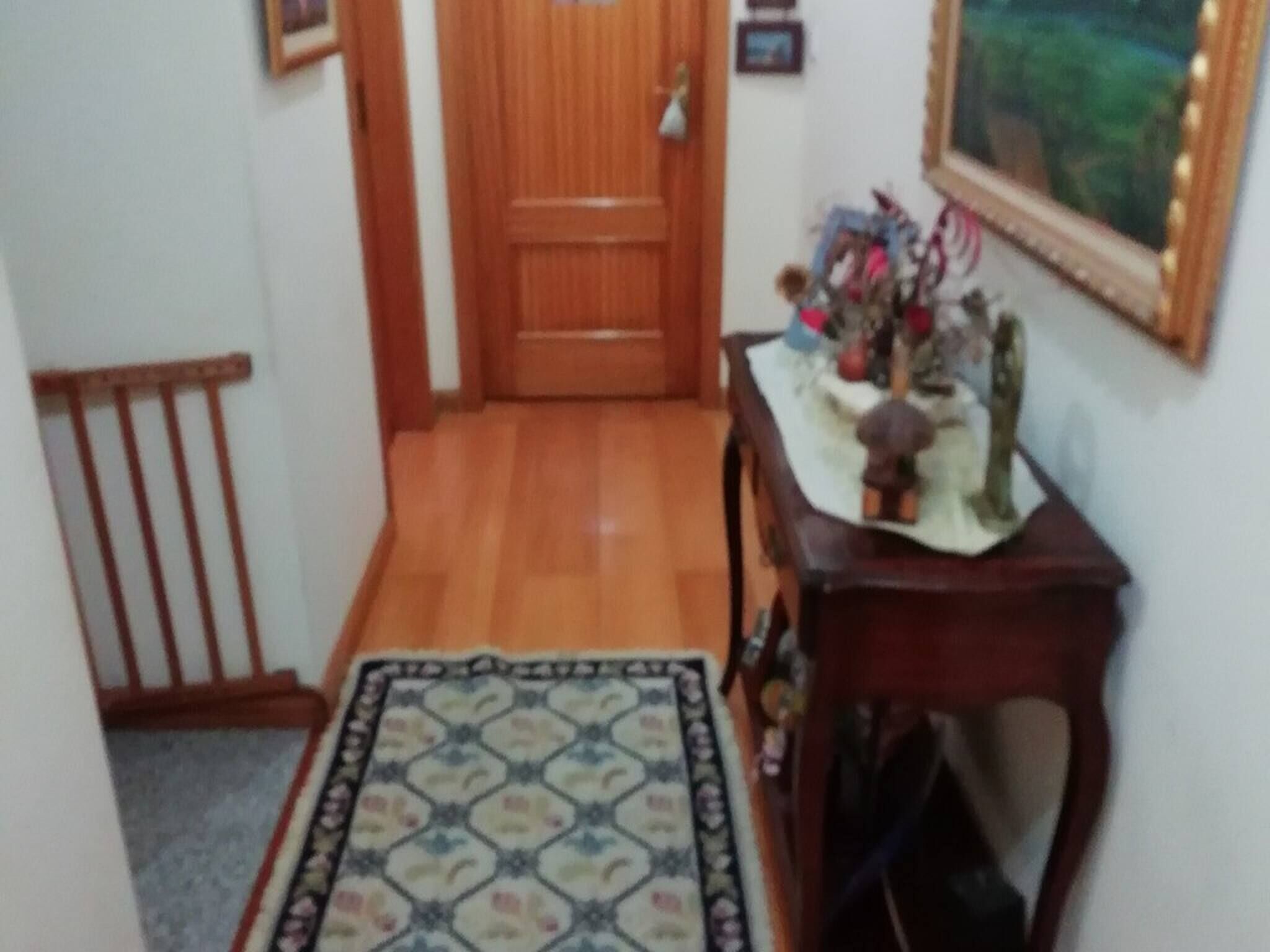 Un couloir avec une porte en bois, un tapis à motifs et une petite table ornée d’objets décoratifs.