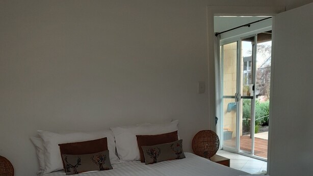 A neatly made bed with white linens and decorative pillows, a dark headboard, and a view of the outdoors through a glass door.