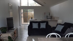A modern living room with a sofa, a dining table with chairs, a TV, and a large window.