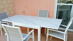 A white outdoor dining set with four chairs and a table, positioned on a brick patio against a peach-colored wall.