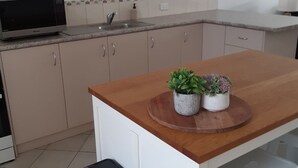 A kitchen with a microwave, sink, cabinets, a wooden countertop, and two potted plants.
