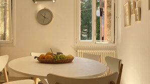 A dining area with a round table, chairs, a clock, and a window with a view of trees and buildings. - Magdalena's House (Venezia)