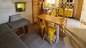 Ein gemütliches Zimmer mit einem Bett, einem Esstisch mit Stühlen, einer kleinen Küchenzeile und einer Holzbalkendecke.