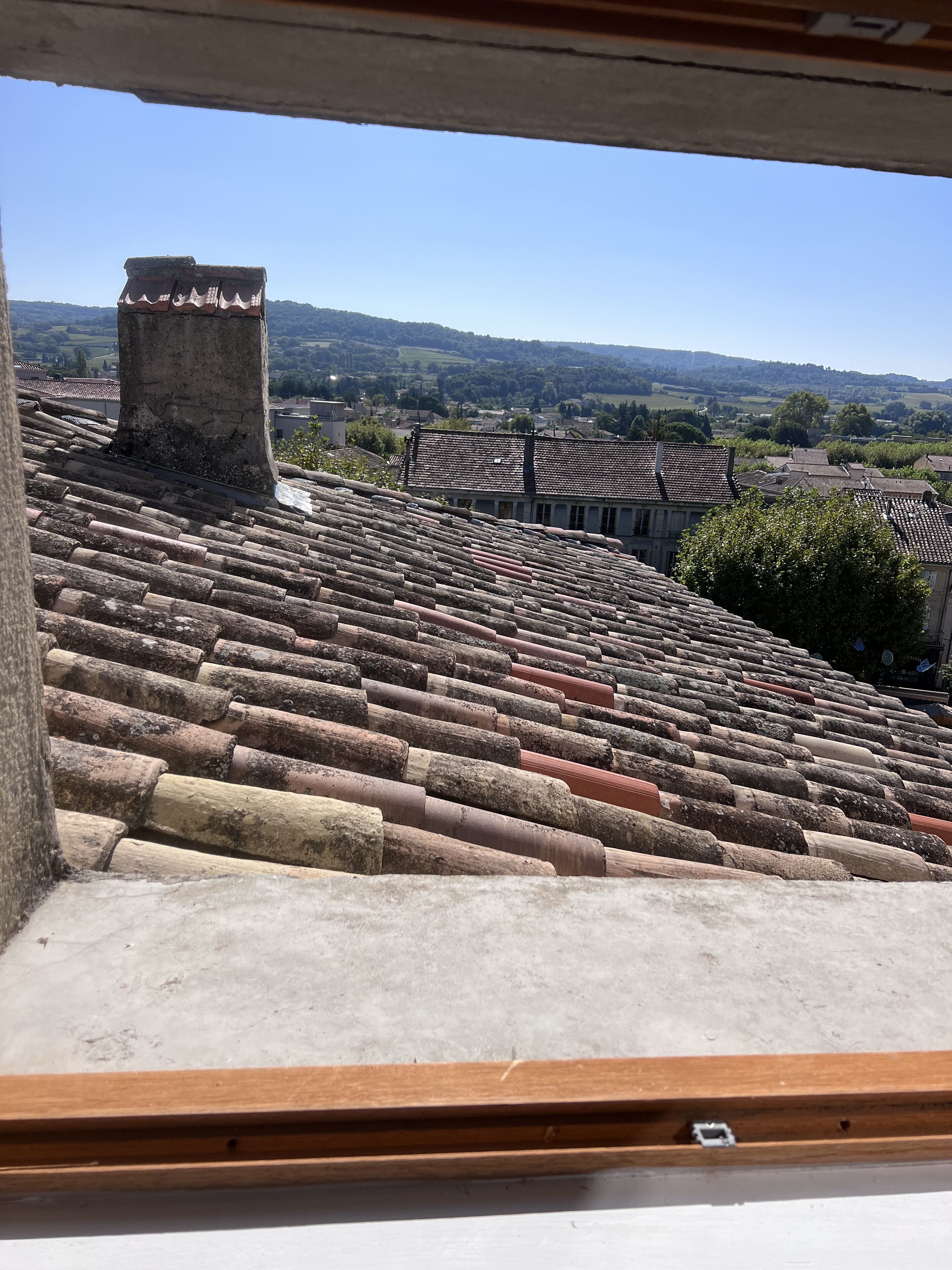 A view of terracotta roof tiles and a chimney from a window.