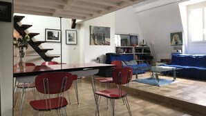 A modern living room with a dining area, featuring a staircase, red chairs, a blue sofa, and a bookshelf. - Au Cœur de Saint Germain ! 80m2 Confortable, Calme et Lumineux Avec vue (Paris)
